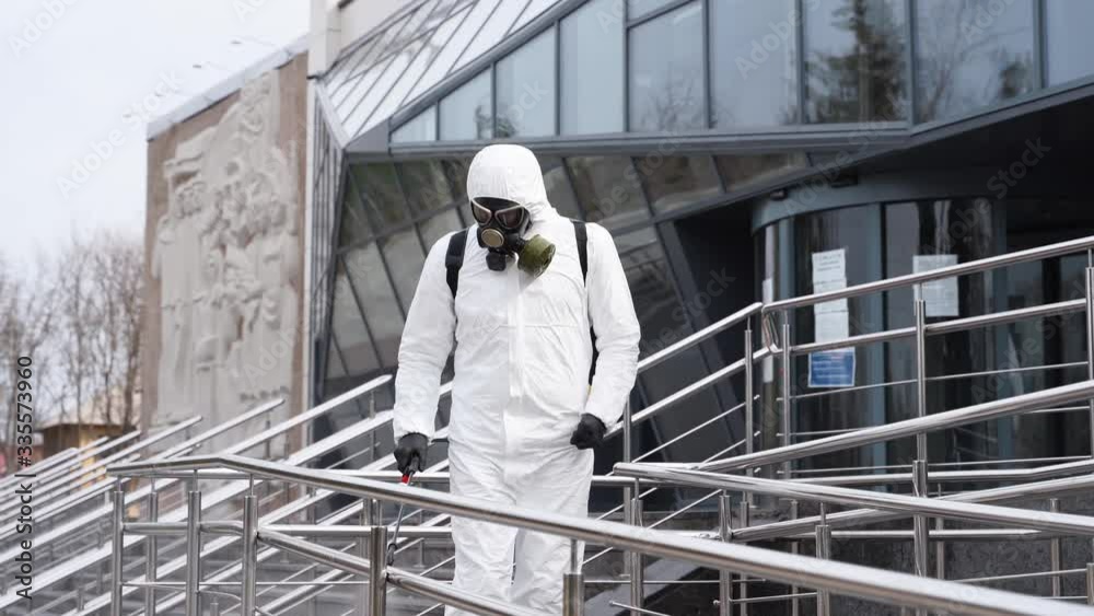 Sanitizer disinfects railing touch surfaces on coronavirus covid-19 quarantine with antibacterial sprayer. Worker in gas mask and hazmat protective suit cleans handrails in city public place. Sanitizer disinfects railing touch surfaces on coronavirus covid-19 quarantine with antibacterial sprayer. Worker in gas mask and hazmat protective suit cleans handrails in city public place.
