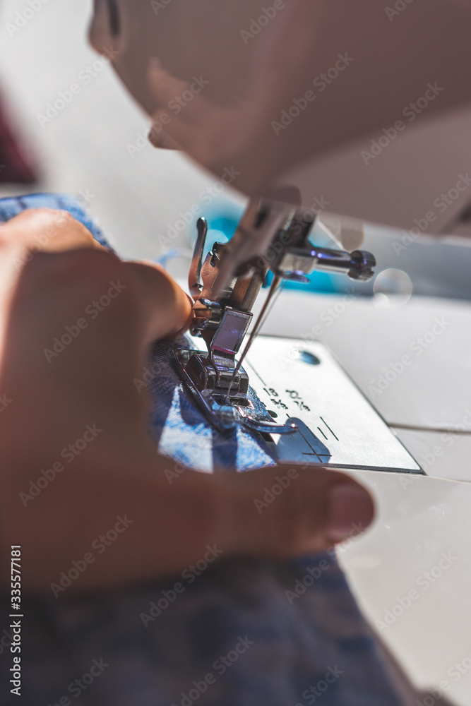 Sewing at home: Woman is sewing at home, close up of sewing needle, textile and hands