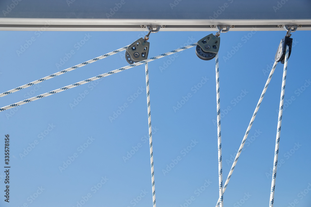 Close-up view of sailboat ropes at sunny weather, pulleys and ropes on the mast, Yachting sport, ship equipment, sea is on background Close-up view of sailboat ropes at sunny weather, pulleys and ropes on the mast, Yachting sport, ship equipment, sea is on background
