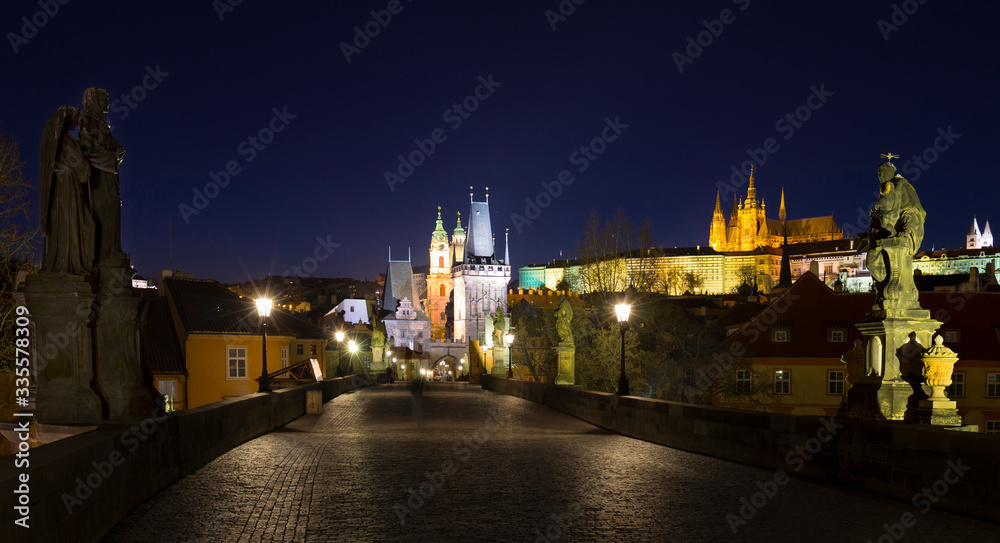 Night colorful Prague gothic Castle with St. Nicholas' Cathedral and Bridge Tower from Charles Bridge with its baroque Statues without People at the time of Coronavirus, Czech Republic