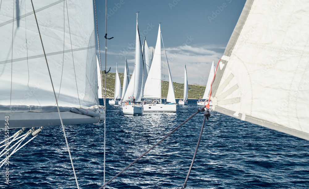 Naklejka premium Sailboats compete in a sail regatta at sunset, race of sailboats, reflection of sails on water, multicolored spinnakers, number of boat is on aft boats, Bright colors