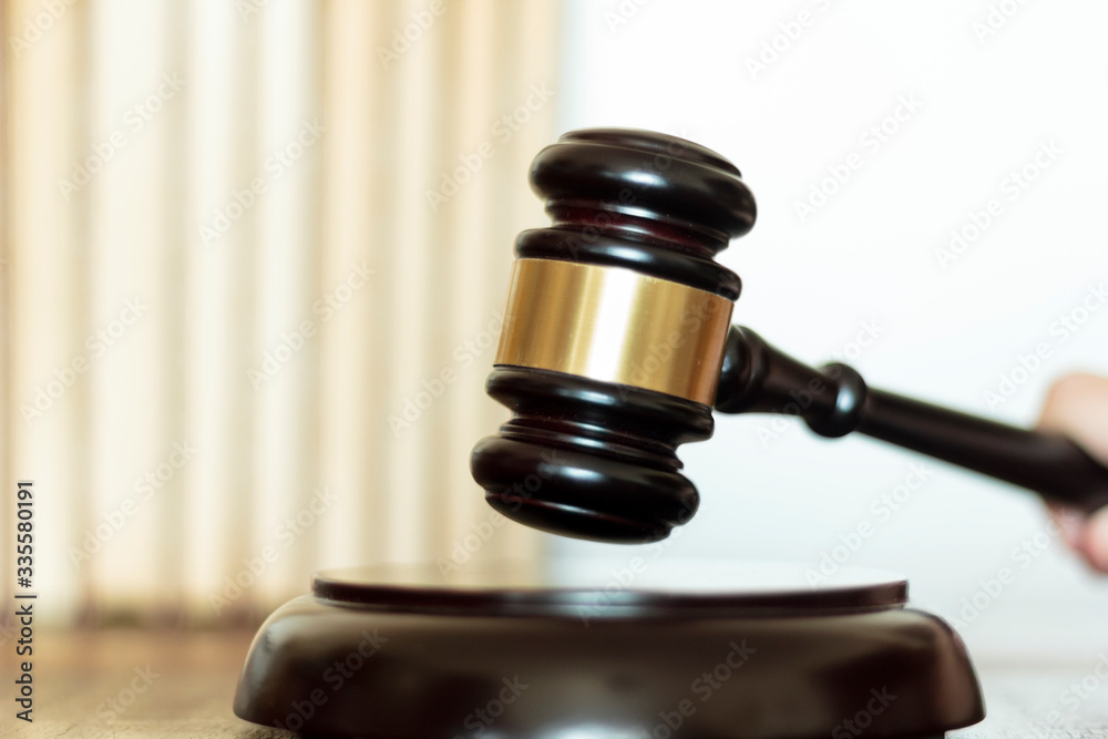 Judge hand's striking the gavel on block with law book on the background