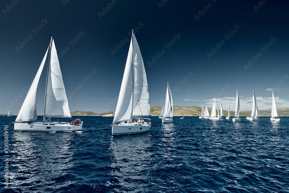 Fototapeta premium Sailboats compete in a sail regatta at sunset, race of sailboats, reflection of sails on water, multicolored spinnakers, number of boat is on aft boats, Bright colors