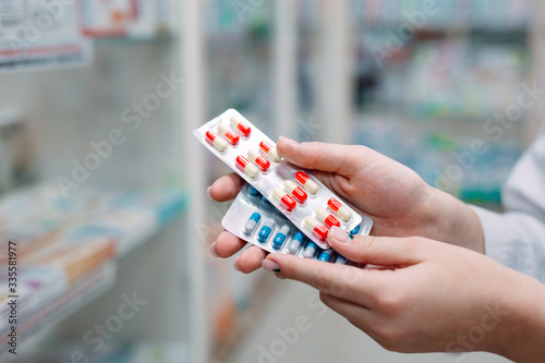 Pharmacist holding medicine box and capsule packs in pharmacy drugstore.