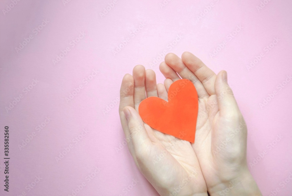 Fototapeta premium Hand holds a red paper heart. Top view. Love and St. Valentines day concept.