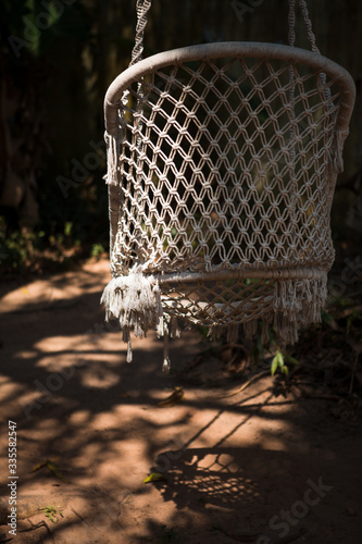 A wicker suspended summer chair hangs in the shade of tropical trees. Close-up weaving photo