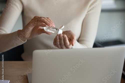 Front close up view young woman sitting at desk with laptop, sanitizing hands with antibacterial alcohol-based gel, cleaning skin, killing corona virus infection, healthcare public awareness concept.