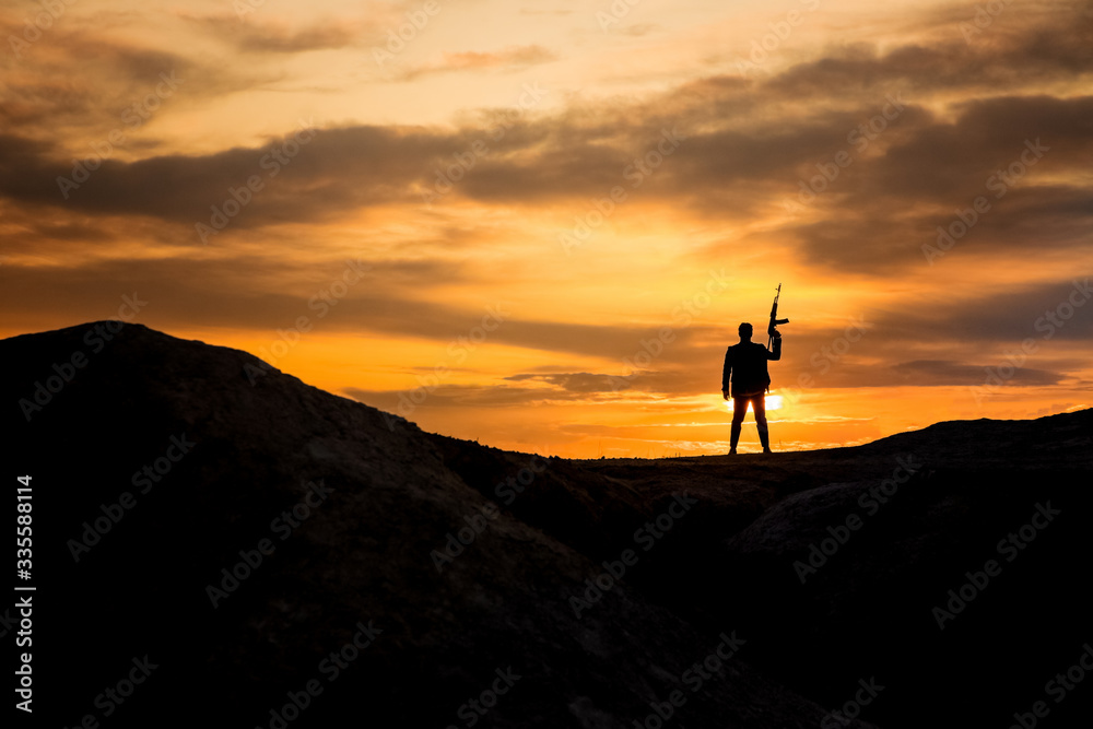 Silhouette of a man with weapon gun at sunset background. War concept.