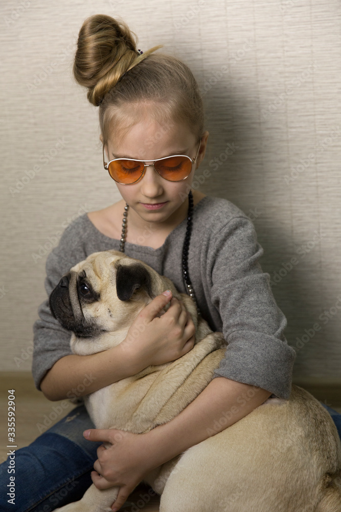 Girl hugs a pug dog. There are sunglasses on the girl. The age of the girl is 9 years. Girl hugs a pug dog. There are sunglasses on the girl. The age of the girl is 9 years.