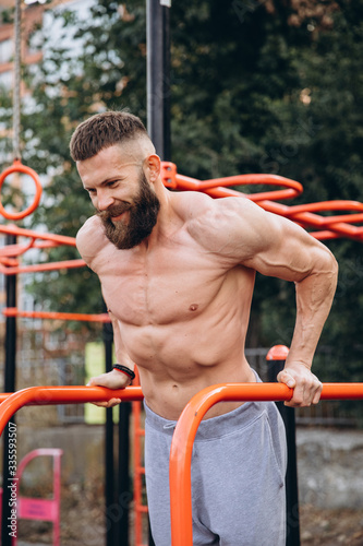 Strong muscular bearded man doing push-ups on uneven bars in outdoor street gym. Workout lifestyle concept.