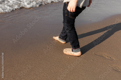 Young boy's feet on beach with sea waves near.