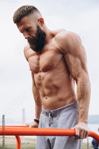 Strong muscular bearded man doing push-ups on uneven bars in outdoor street gym. Workout lifestyle concept.