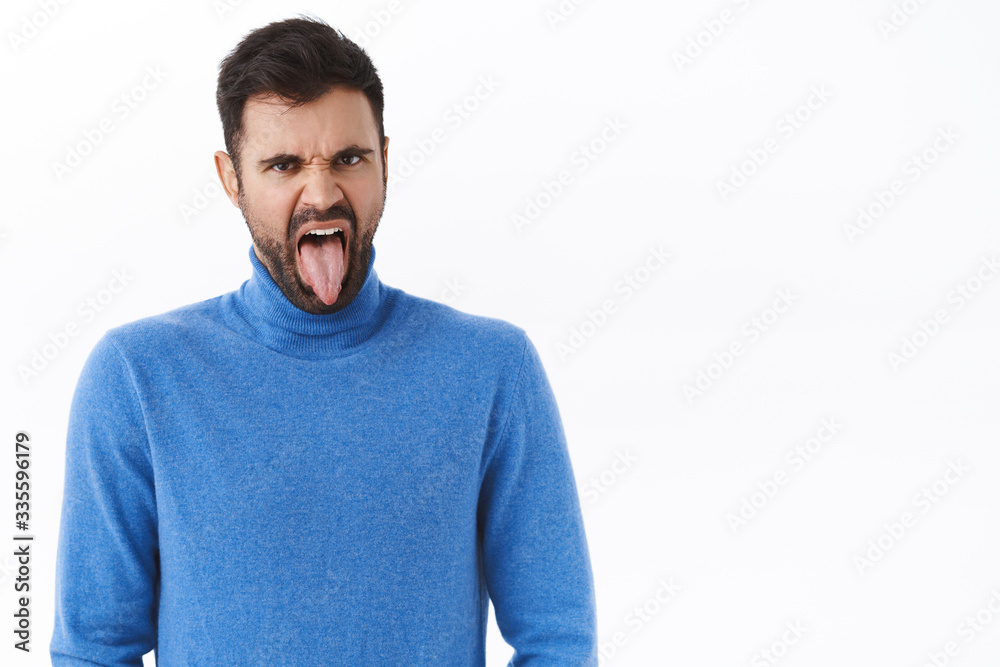 Obraz premium Portrait of disgusted and displeased grimacing funny bearded man, showing tongue and frowning bothered, see something awful, taste bad cooked food, standing disappointed white background