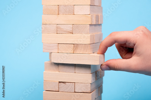 The tower is made of wooden blocks. Jenga. Hand of man. Close up. On a blue background