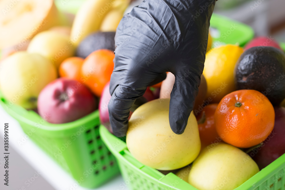 A hand in rubber gloves takes fruit from a store shelf. Coronavirus epidemic concept.