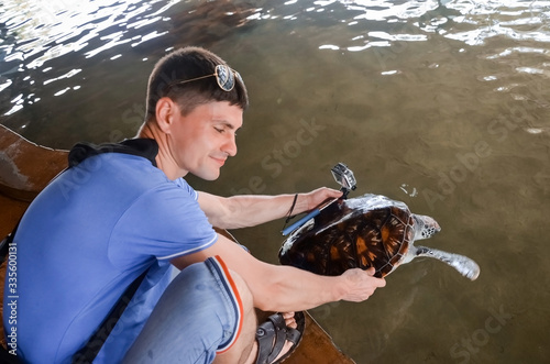 Photography Young brunette guy with camera releases turtle into water, volunteer saves turtles, animal protection, boy takes pictures of turtle