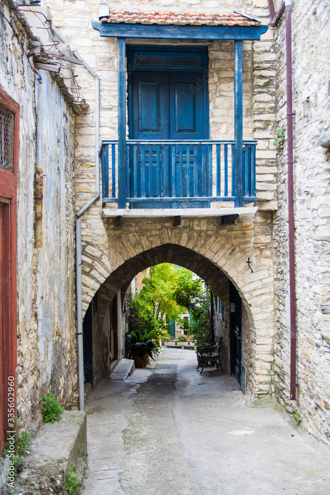 Cyprus village Lefkara. View of a village stony street decorated by green bushes. Street go through an arch with balcony with a blue wooden door.