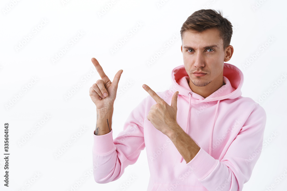 Close-up portrait of determined, thoughtful young confident man with blond hair, pink hoodie encourage take a moment, visit site and learn info, showing way, look camera and point upper left corner Close-up portrait of determined, thoughtful young confident man with blond hair, pink hoodie encourage take a moment, visit site and learn info, showing way, look camera and point upper left corner