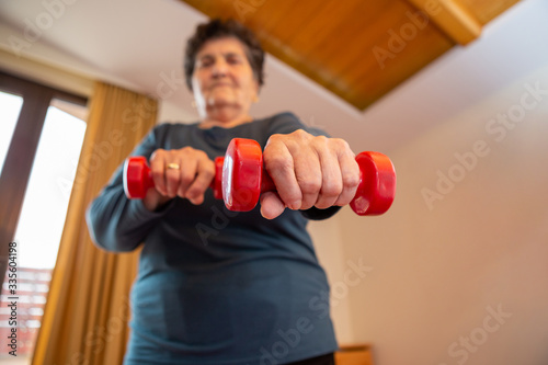 Focus on the hand of a senior woman who has red weights in her hands. She strives to keep her body in good physical condition and exercise daily.
