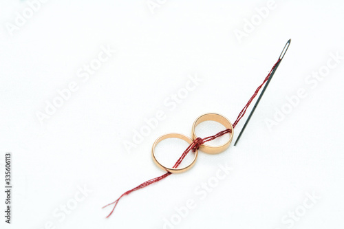On a white background two gold wedding rings are connected by a red thread coming from a sewing needle. Concept - betrothal, wedding, love for life photo