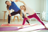 Young woman with her adorable daughter practicing yoga at home during coronavirus quarantine