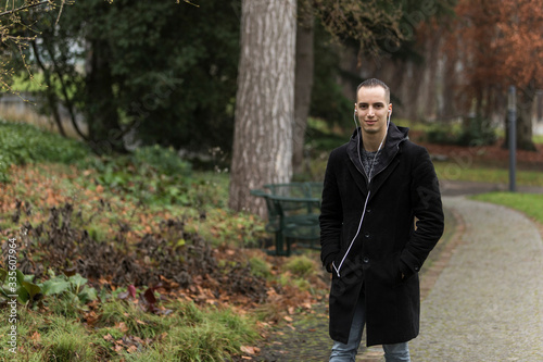 Young Man Walking Through Park in Autumn Listening to Earphones
