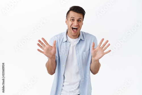 Cheerful handsome happy man make jazz hands, waving empty palms and smiling rejoicing, saying hello or hi to friend, informal greeting concept, pleased to meet neighbour, white background © Cookie Studio