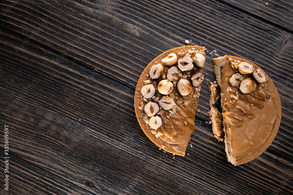 Delicious tart with caramel and hazelnuts on the wooden background, halved. Top view, flat lay, natural light Delicious tart with caramel and hazelnuts on the wooden background, halved. Top view, flat lay, natural light