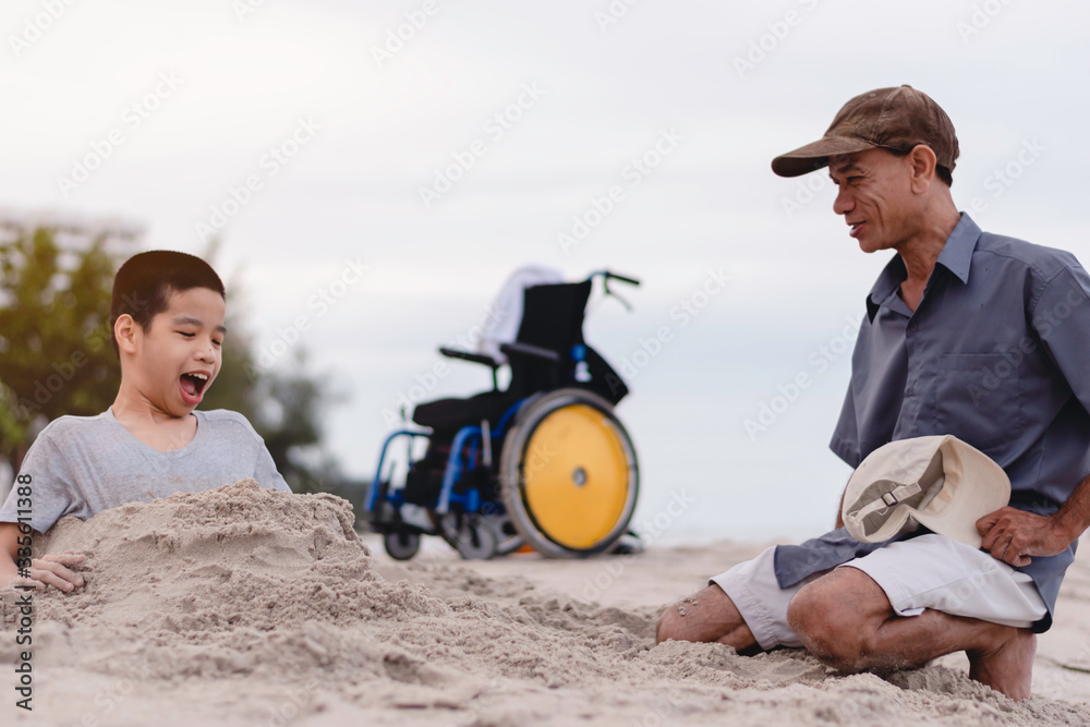 Asian special child on wheelchair and his father on the beach with daylight, They are happiness in holidays with the travel, Life in the education age of disabled children, Happy disabled kid concept.