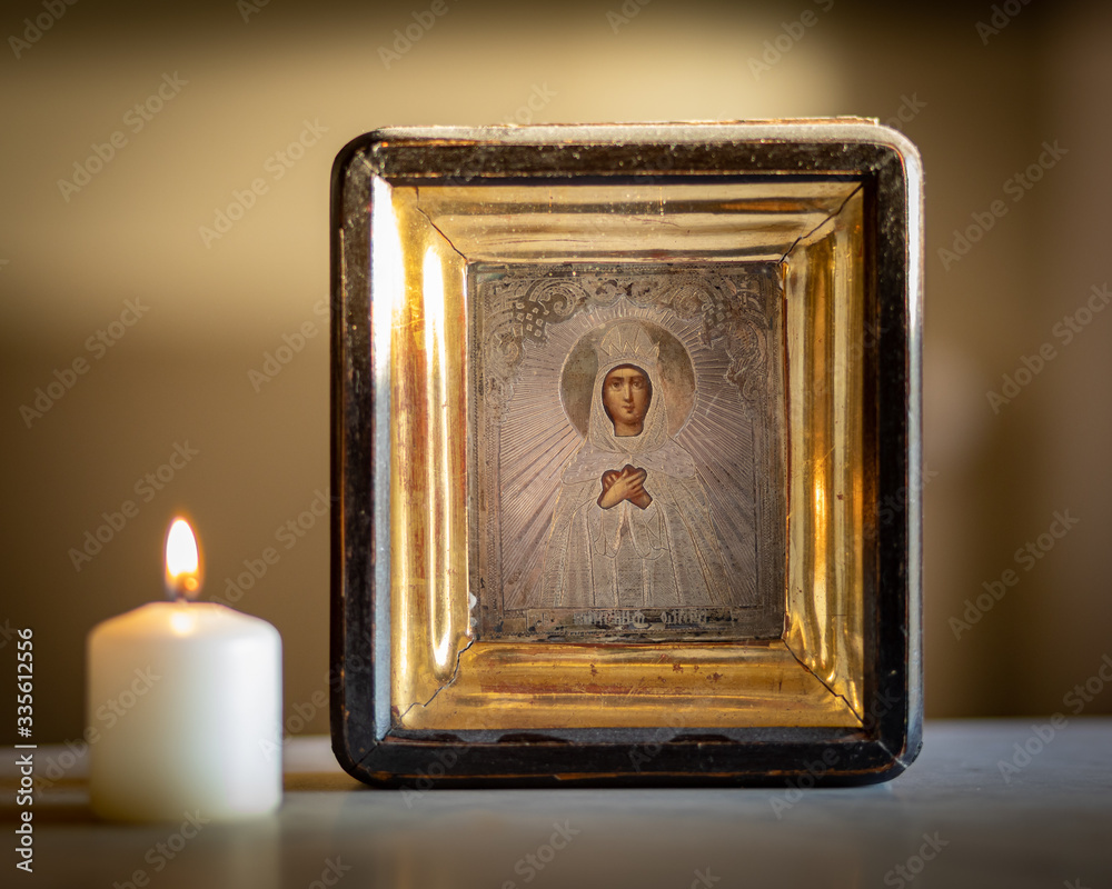 A candle burning in front of an icon of holy mother and child