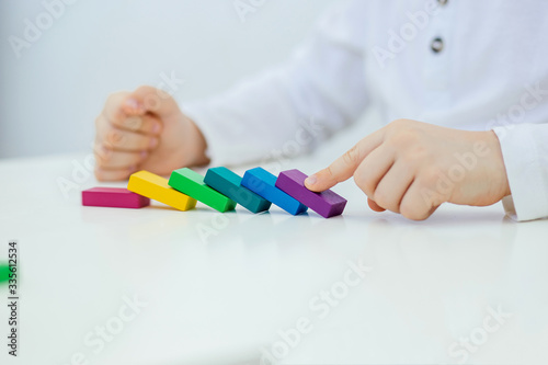 Building items in a single row. Concept of diagnostics of children's autism. A child plays with a colored wooden construction tool. Close.