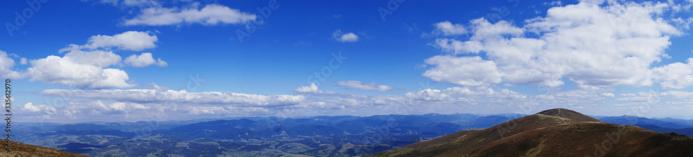 Panorama from Mount Hymba on a sunny day in late August. Top view of small mountains in the distance. Hanging clouds over the mountains. Carpathians, Ukraine, Europe.