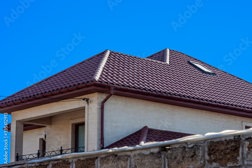Brown Tiled roof of the house with windows on a background of blue sky