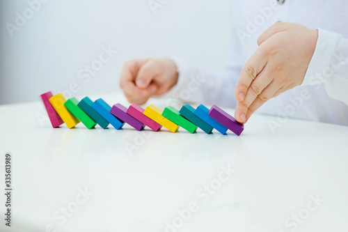 Building items in a single row. Concept of diagnostics of children's autism. A child plays with a colored wooden construction tool. Close.