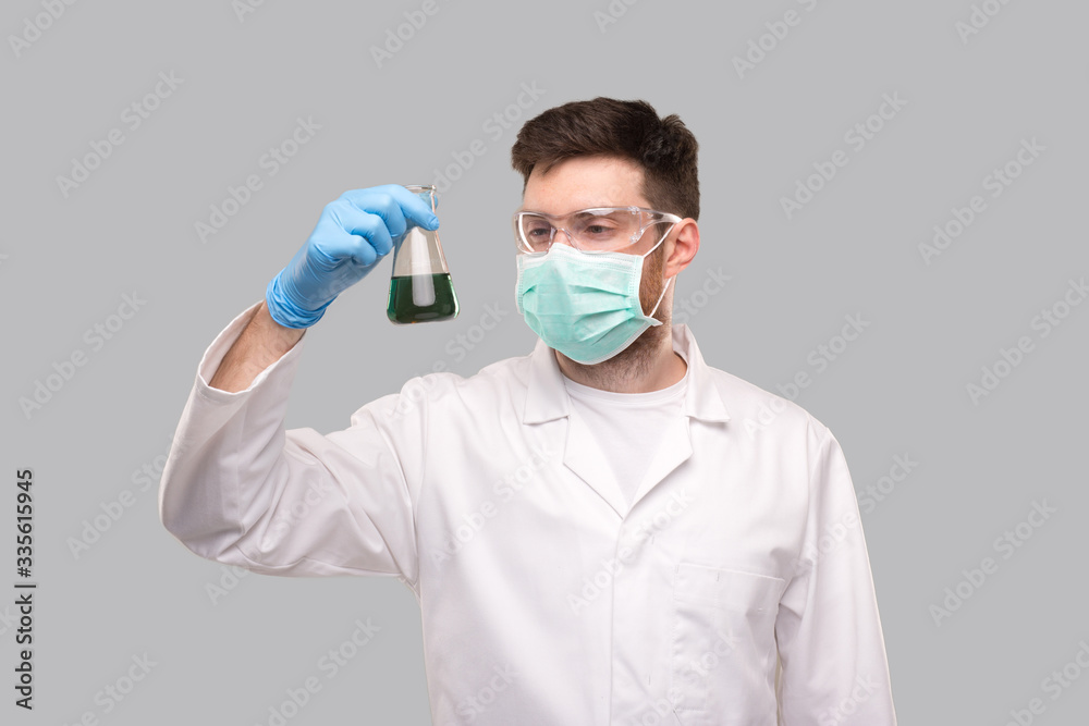 Male Doctor Wearing Medical Mask and Glasses Watching Flask with Colorfull Liquid. Science, Medical, Virus Concept Male Doctor Wearing Medical Mask and Glasses Watching Flask with Colorfull Liquid. Science, Medical, Virus Concept