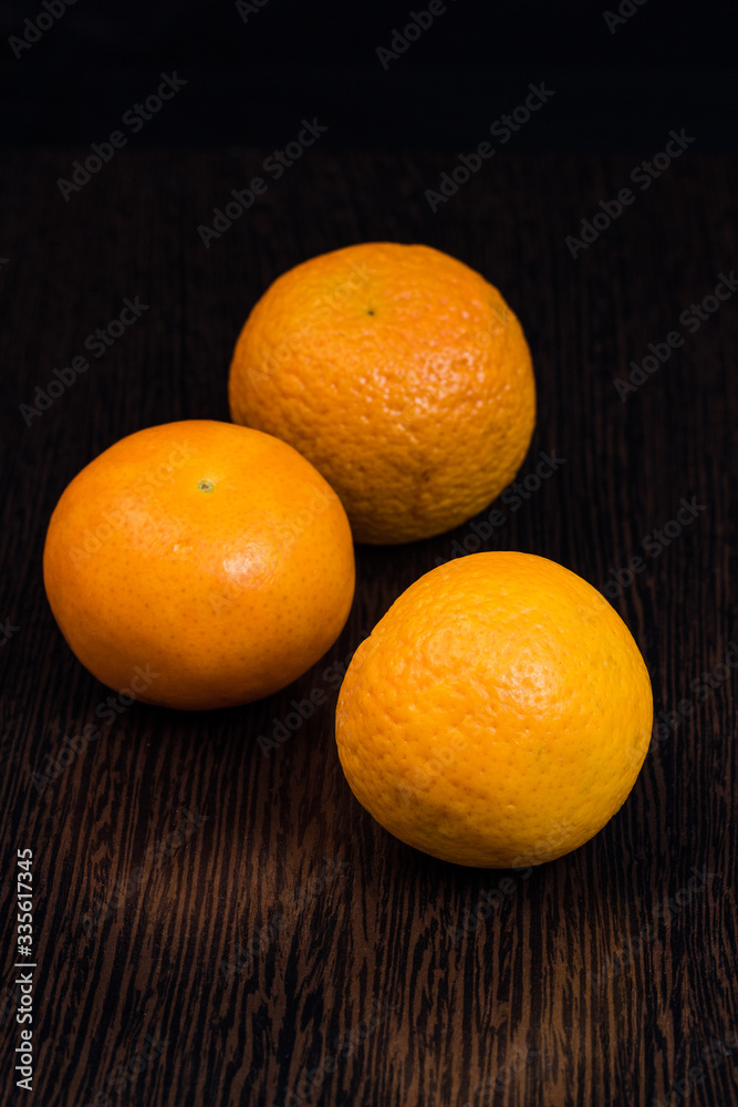 three mandarins on a dark brown background three mandarins on a dark brown background
