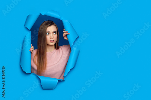 Portrait of frowning caucasian woman looking with upset face expression aside posing in blue paper hole. copy space. © producer