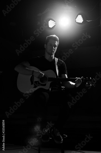 A young handsome guy of European appearance plays an acoustic guitar and sits on a chair. Black and white photography.