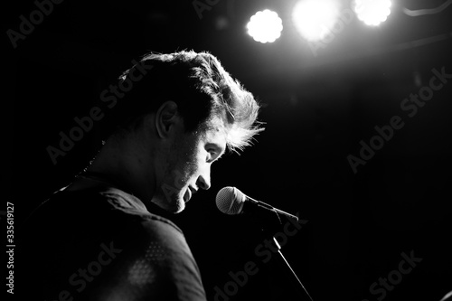 Young handsome guy emotionally sings and speaks into the microphone. Black and white photography