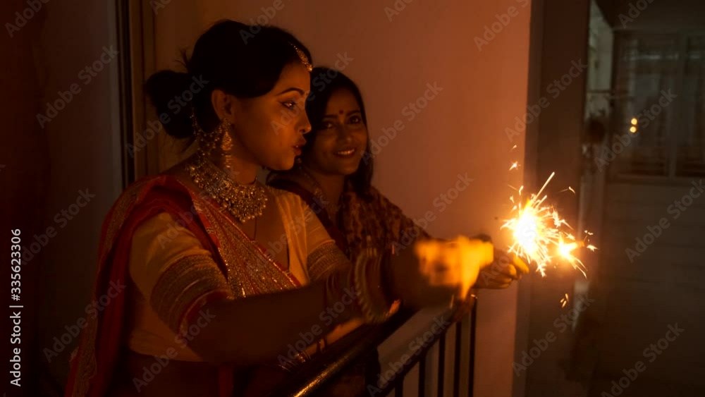 Two young and beautiful Indian Bengali women in Indian traditional dress are celebrating Diwali with fire crackers on a balcony in darkness. Indian lifestyle and Diwali celebration Two young and beautiful Indian Bengali women in Indian traditional dress are celebrating Diwali with fire crackers on a balcony in darkness. Indian lifestyle and Diwali celebration
