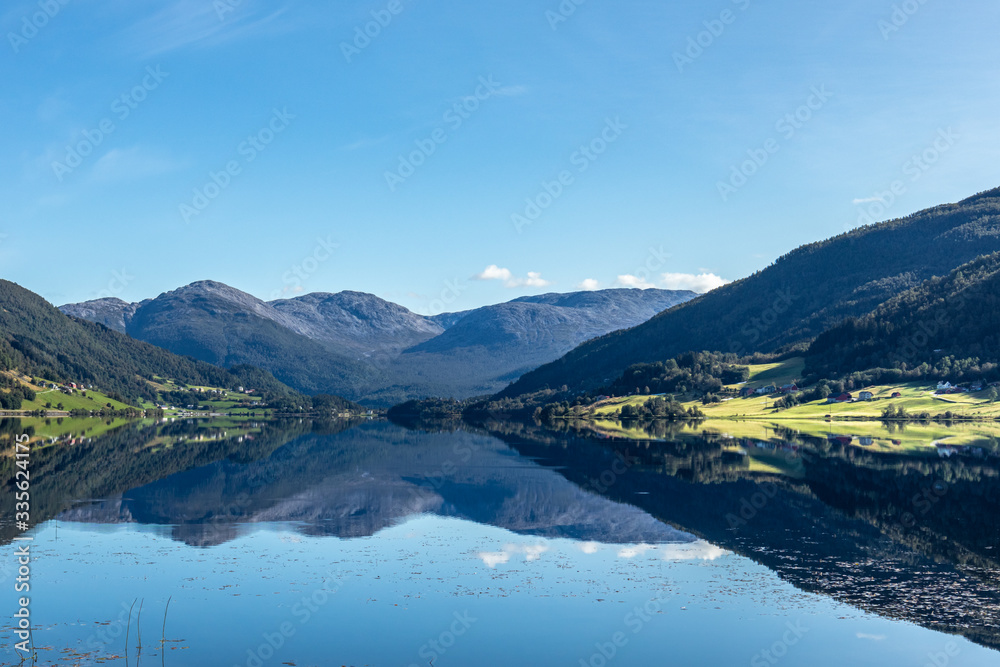 Norway mountains lake mirror on sunny day landscape. Hills reflection on water surface, blue sky, bright colors 