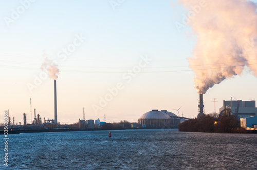 Smoking chimneys of industrial enterprise in the city on the river bank.
