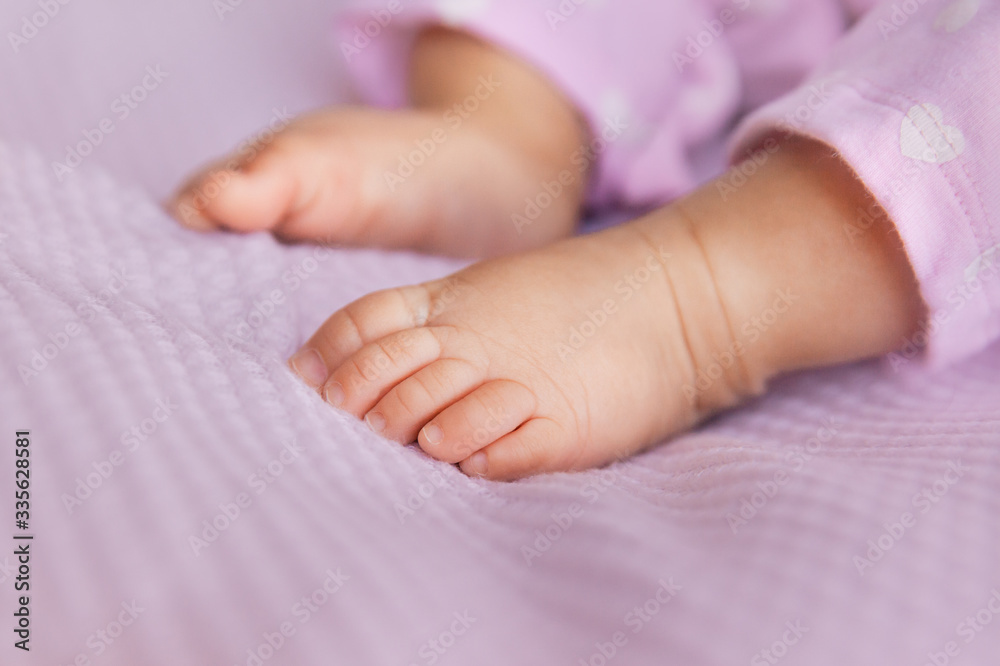 Newborn baby girl legs on lilac background, closeup of infant barefeet Newborn baby girl legs on lilac background, closeup of infant barefeet