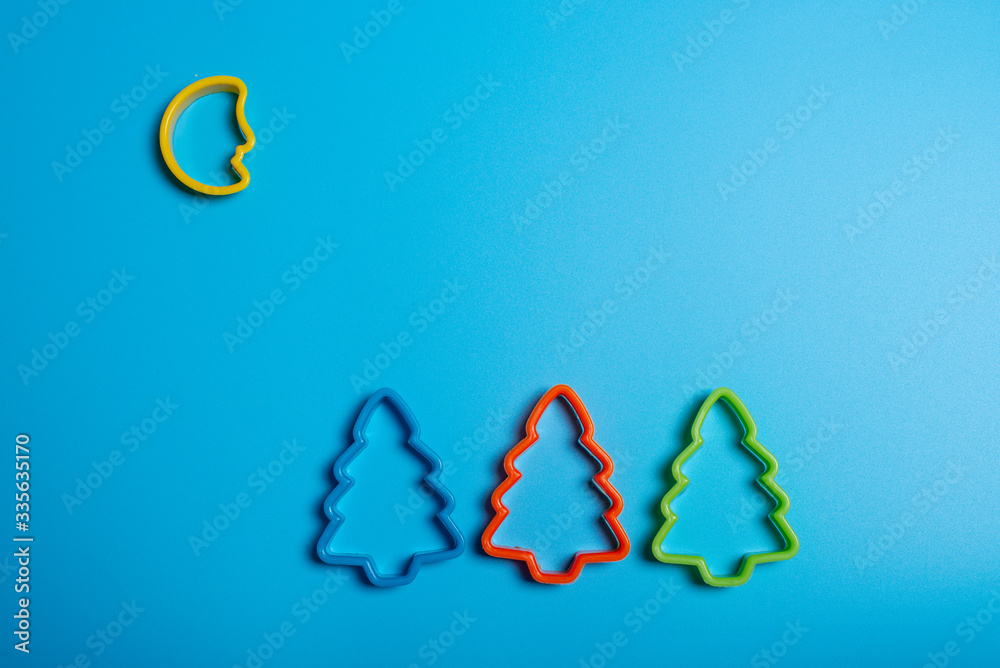 Colored cookie cutters for the preparation of a three Christmas tree and the moon on a blue background. Culinary concept. Flat lay with copyspace.