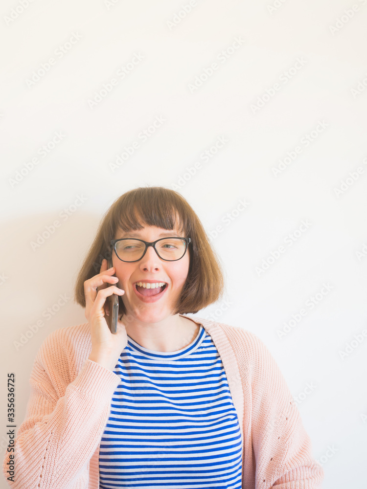 Laughing young woman with eyeglasses and brown hair wearing pastel color clothes using smartphone. Study, work from home, phone call concept Laughing young woman with eyeglasses and brown hair wearing pastel color clothes using smartphone. Study, work from home, phone call concept
