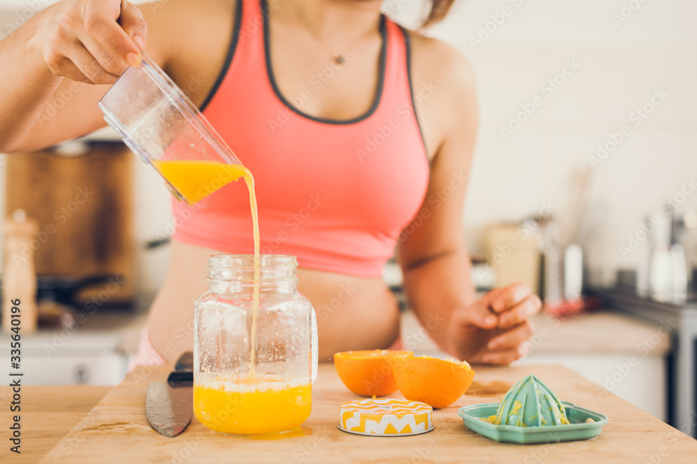 Young woman in sportswear pouring freshly squeezed orange juice in a jar. Young woman in sportswear pouring freshly squeezed orange juice in a jar.