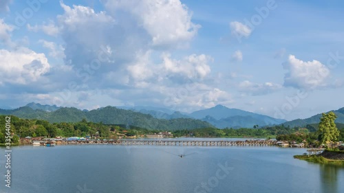 Mon Bridge, longest wooden bridge in country over Songalia River and reservoir over dam in Sangkhlaburi during sunny day, Kanchanaburi, Thailand; zoom in - Time Lapse photo