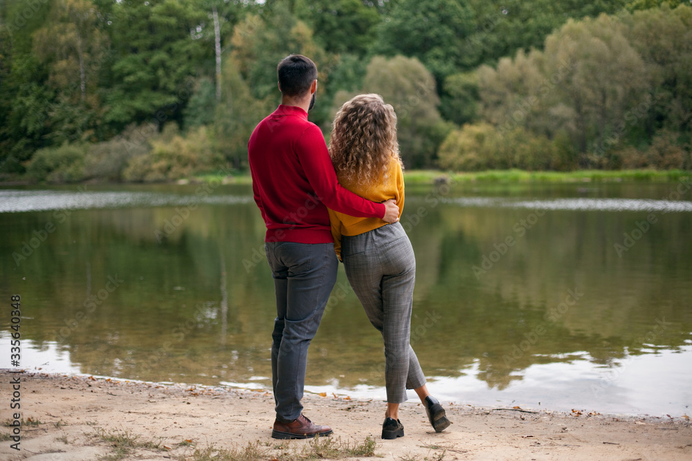 Guy and girl stand on the shore of the lake in the park in autumn