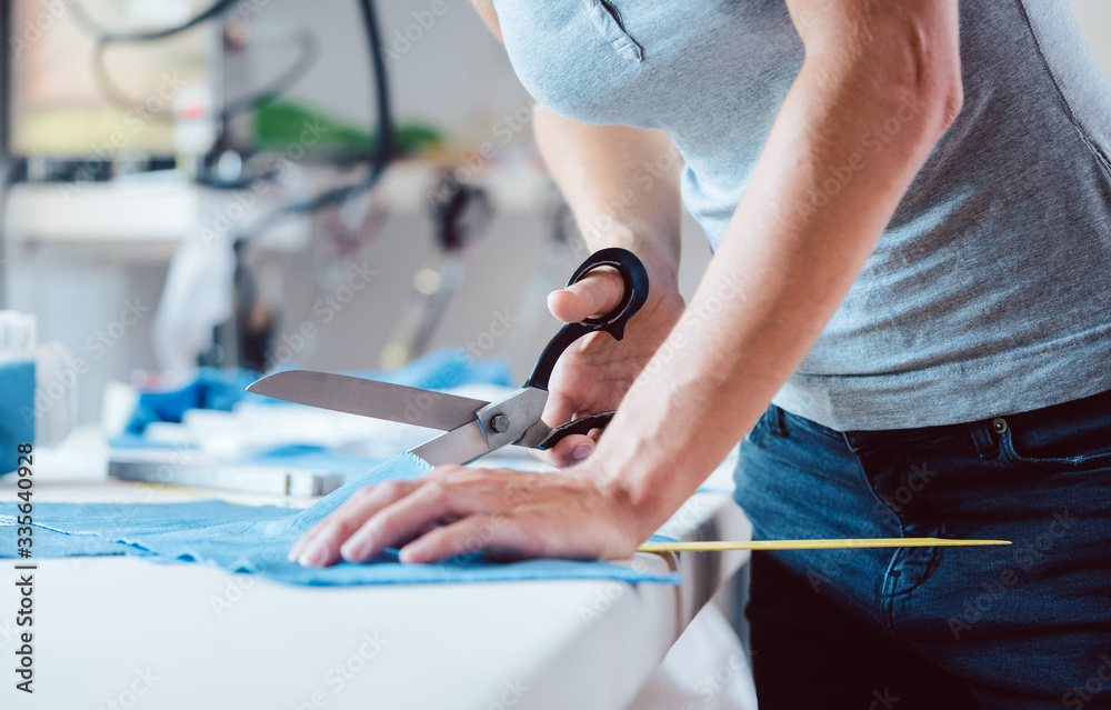 Woman cutting fabric with tailor scissors on tailor’s table