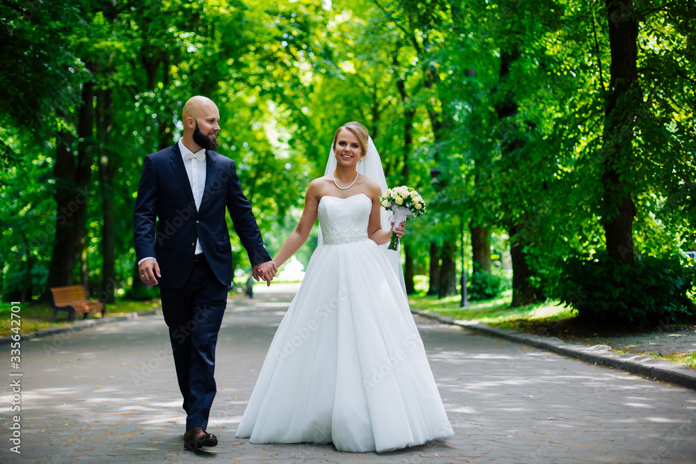 A young and beautiful bride and her husband is standing in a summer park with bouquet of flowers A young and beautiful bride and her husband is standing in a summer park with bouquet of flowers